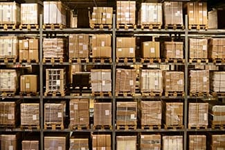 Rows of densely packed shelves in a warehouse filled with cardboard boxes and goods on pallets, indicative of a well-stocked inventory.